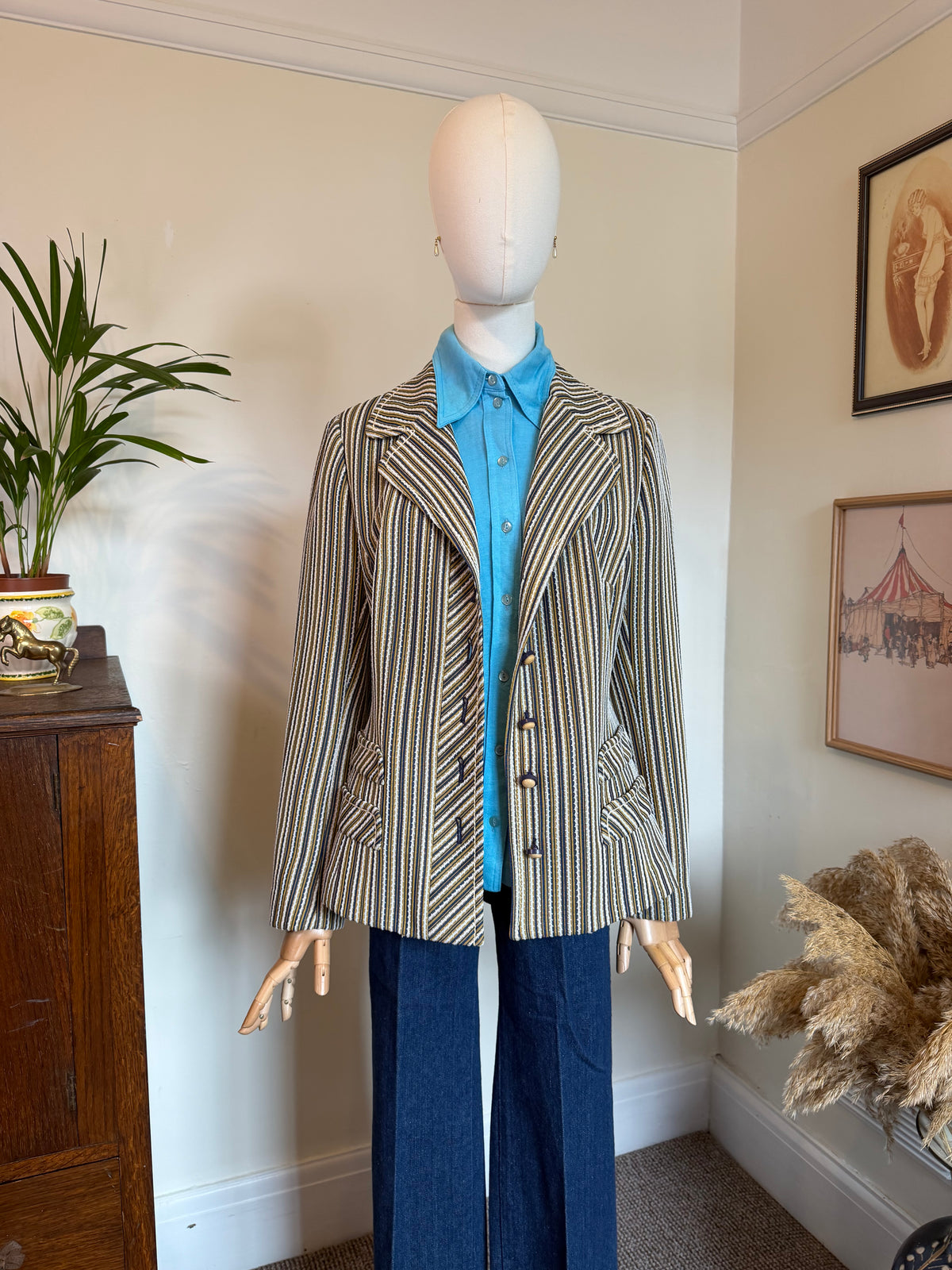 A vintage striped blazer displayed on a mannequin torso, styled with a bright blue collared shirt and navy wide-leg trousers in a home interior setting.