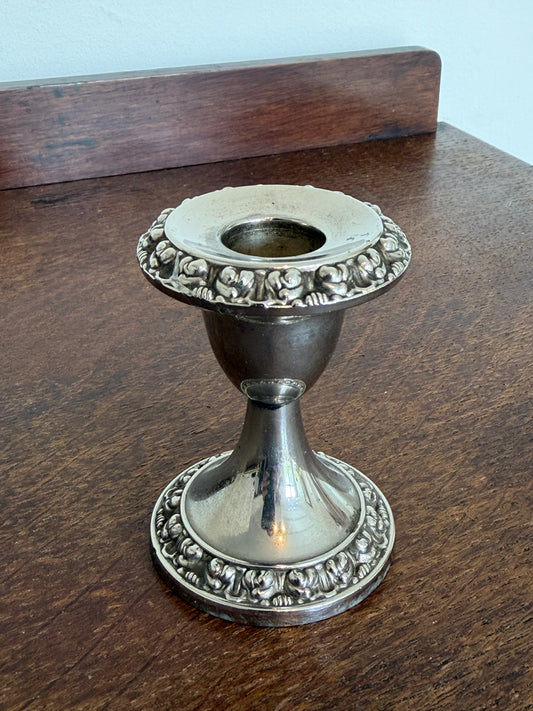An ornate silver-toned metal wall-mounted candle holder or candlestick mount with decorative floral relief borders, shown attached to a dark wood surface.