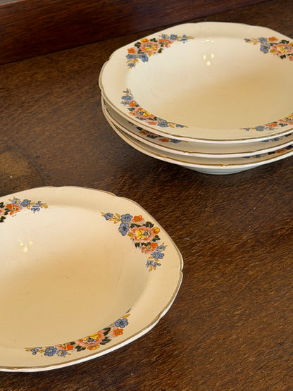 Set of four vintage John Maddock & Sons Ivory Ware shallow soup bowls dating from the 1940s–1950s, featuring a cream ground, colourful floral border in blue, pink and orange, and fine gold edging, arranged on a dark wooden surface.