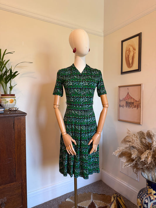 Vintage handmade green floral dress with a fitted waist, v neckline, short sleeves and tiered skirt, featuring a delicate blue and white floral stripe print, displayed on a mannequin.