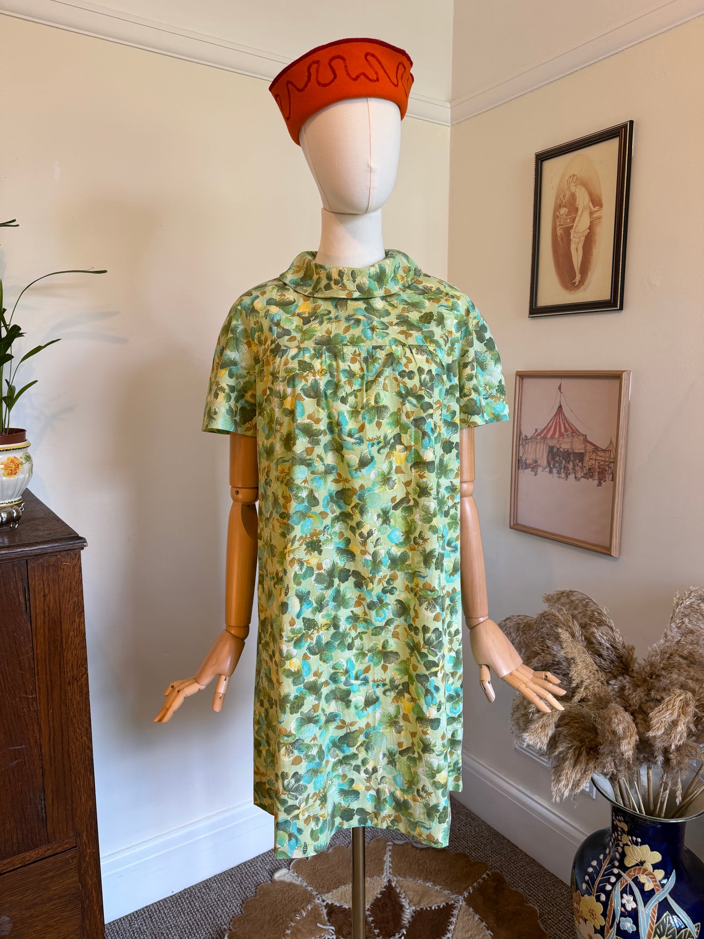 Vintage 1960s green floral shift dress with a painterly turquoise and olive botanical print, roll collar neckline and short sleeves, displayed on a mannequin.