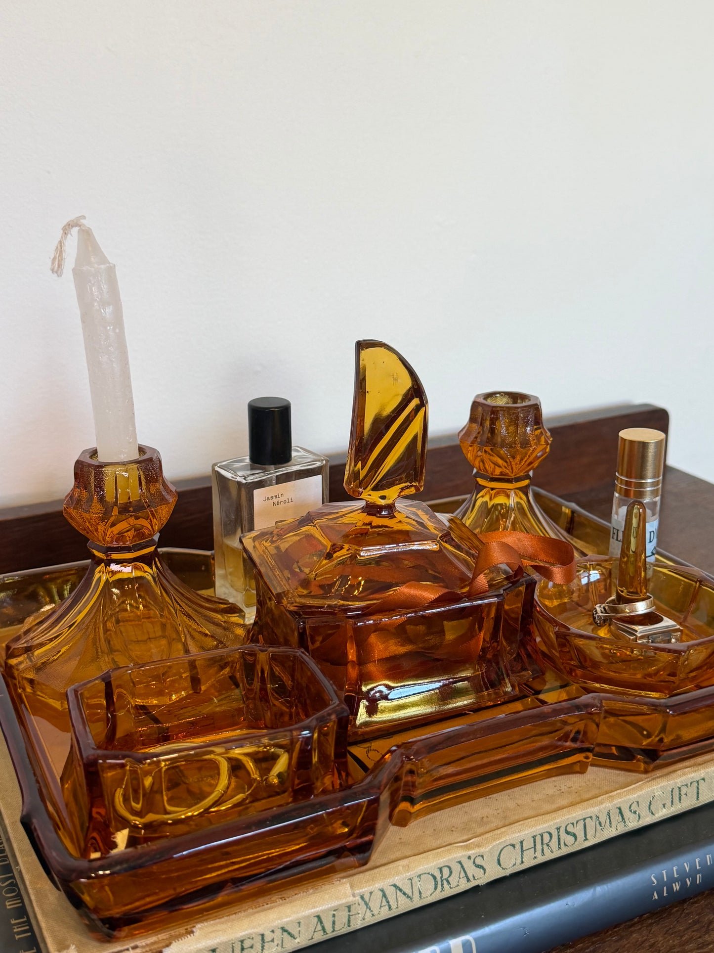 Vintage amber glass vanity set consisting of a large rectangular tray, lidded trinket box, two matching candlestick holders, a ring holder and small dish, styled with jewellery and perfume bottles on a dark wooden surface.