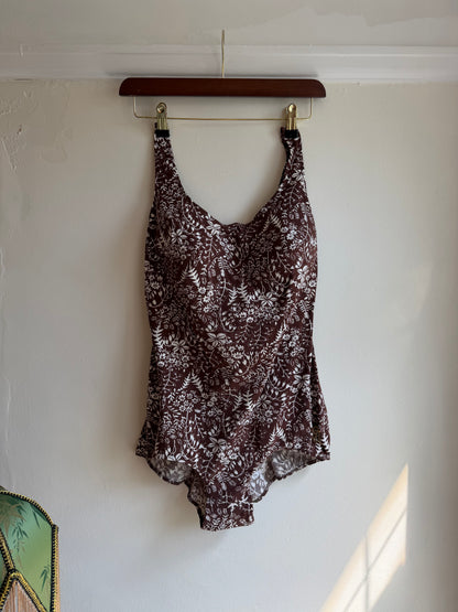 A sleeveless scoop-neck top with a brown and white abstract floral pattern, hanging on a wooden hanger against a white wall.