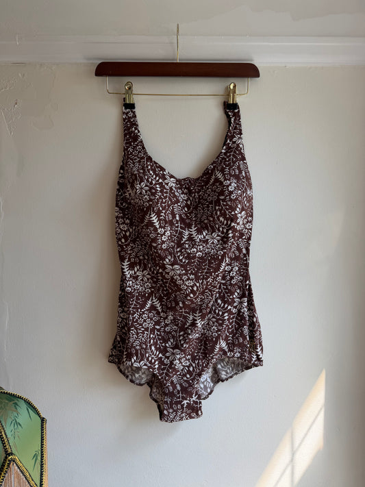 A sleeveless scoop-neck top with a brown and white abstract floral pattern, hanging on a wooden hanger against a white wall.