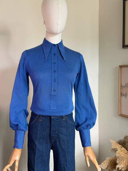 A mannequin wearing a bright blue western style long-sleeve button-front shirt with a pointed collar and dark blue jeans, photographed indoors against a light wall.