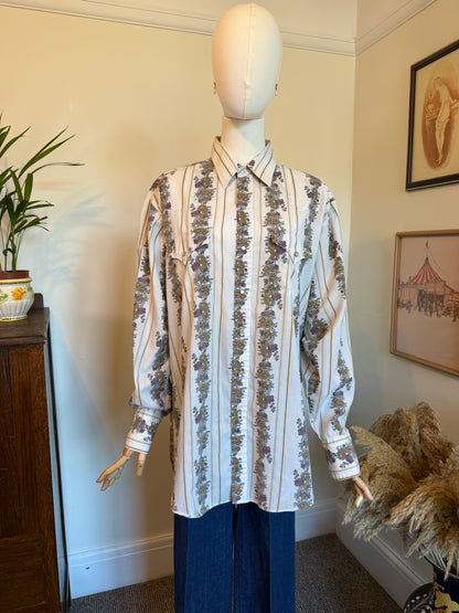 A long-sleeve button-up shirt with vertical stripes and floral motifs, displayed on a mannequin in an indoor room setting.