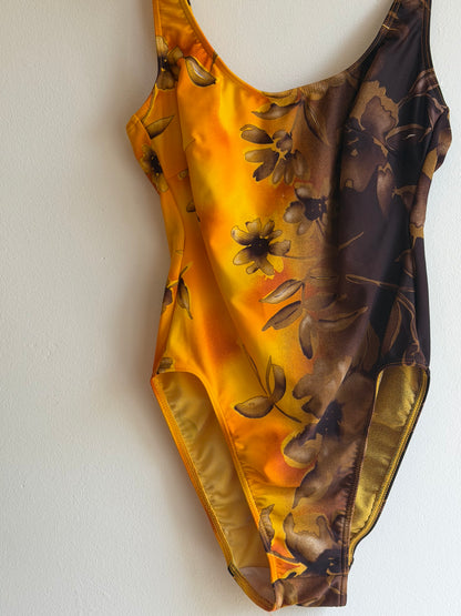 A close-up of a satin-like garment or fabric accessory with a floral print, showing a gradient from dark brown at the top to bright yellow-gold at the bottom, laid flat against a plain white background. Vintage late 1970s mustard yellow and chocolate brown floral one-piece swimsuit with colour-block design.