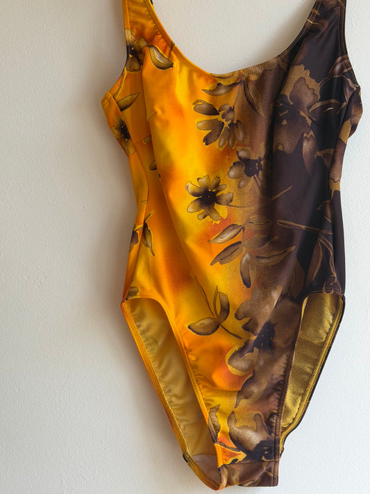 A close-up of a satin-like garment or fabric accessory with a floral print, showing a gradient from dark brown at the top to bright yellow-gold at the bottom, laid flat against a plain white background. Vintage late 1970s mustard yellow and chocolate brown floral one-piece swimsuit with colour-block design.