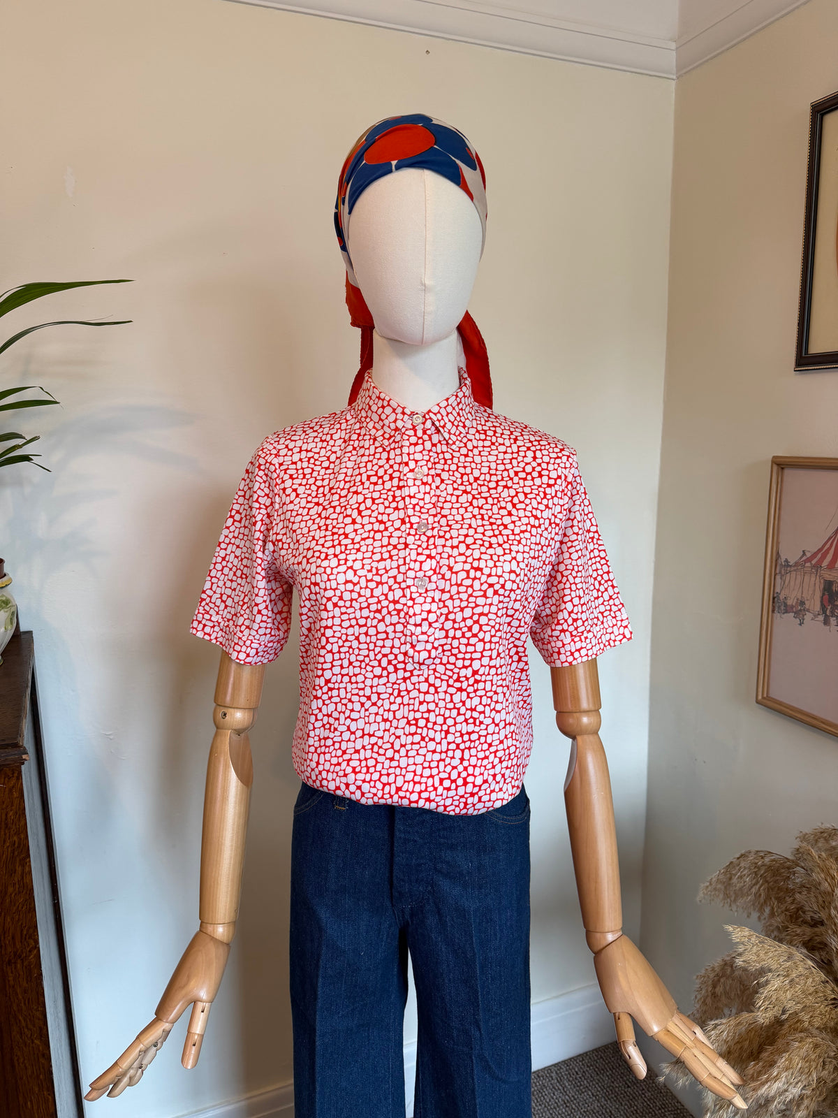 Vintage red and white geometric print blouse with pointed collar, short sleeves and front button fastening, styled with dark blue jeans.