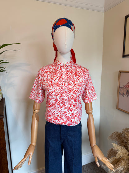 Vintage red and white geometric print blouse with pointed collar, short sleeves and front button fastening, styled with dark blue jeans.