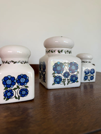Set of three vintage Taunton Vale Pottery ceramic canisters in cream glaze with bold blue floral designs and rounded lids, photographed on a wooden surface. One large square storage jar is accompanied by two smaller matching shakers, with maker’s mark visible on the underside.