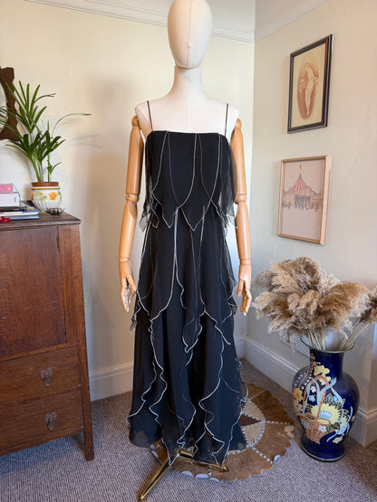 Vintage 1970s Vera Mont black chiffon evening gown with delicate spaghetti straps, cascading layered ruffles trimmed in silver and a flowing maxi-length silhouette displayed on a mannequin.