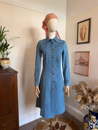 Vintage 1970s blue denim midi dress with a fitted silhouette, button-through front, pointed collar and Western-inspired yoke detailing, displayed on a mannequin.