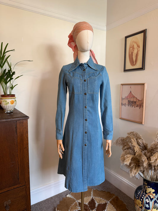 Vintage 1970s blue denim midi dress with a fitted silhouette, button-through front, pointed collar and Western-inspired yoke detailing, displayed on a mannequin.