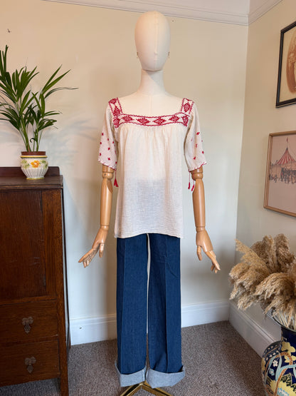 Vintage 1970s white cotton tunic with red embroidered neckline, sleeves and tassel details, displayed on a mannequin.