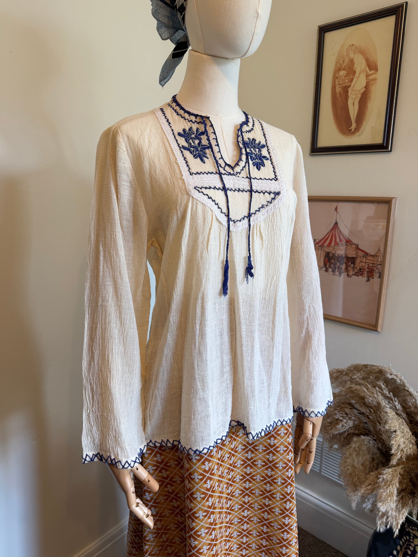 Vintage ivory cotton folk blouse with cobalt blue floral embroidery, tassel tie neckline and long sleeves, displayed on a mannequin.