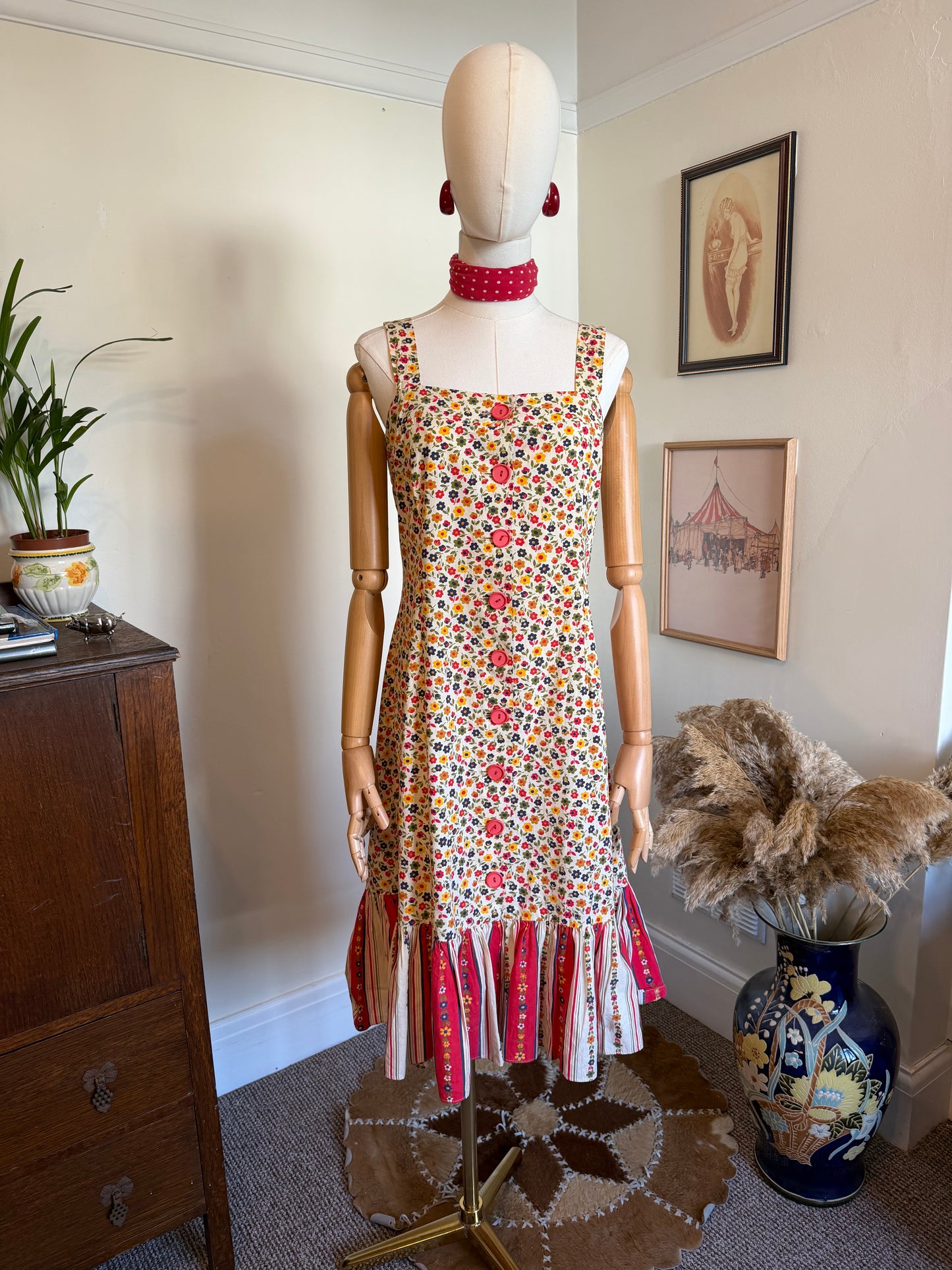 Vintage 1970s floral sundress with a cream ditsy flower print, square neckline, pink button-front detail and contrasting striped ruffle hem in pink and cream, displayed on a mannequin.