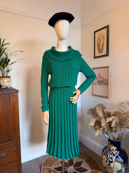 Vintage 1970s emerald green ribbed knit two-piece set comprising a long-sleeved cowl-neck jumper and matching pleated midi skirt, displayed on a mannequin wearing a black beret.