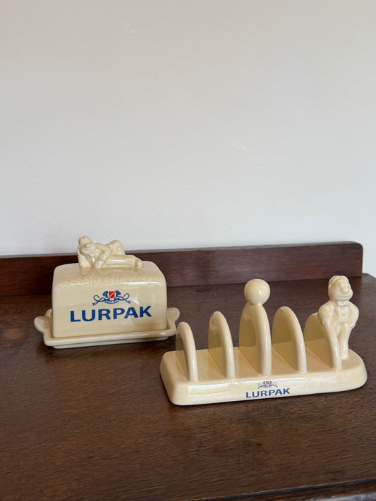A cream-colored ceramic LURPAK butter dish and matching five-spoke toast rack set on a dark wooden table against a plain light wall.