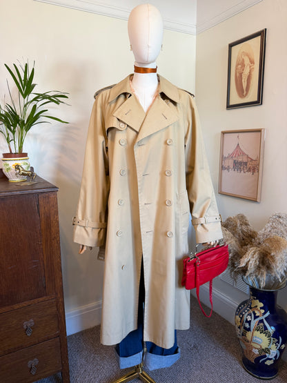 Vintage 1980s beige Peter Brown trench coat displayed on a mannequin, featuring a double-breasted front, wide collar, belted waist, shoulder epaulettes and cuff straps.