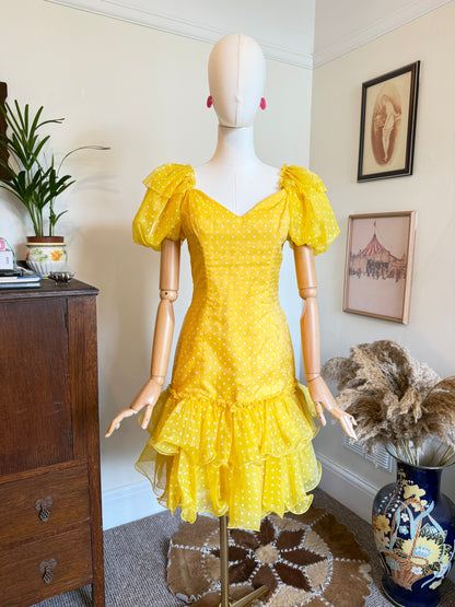 
Vintage bright yellow polka dot rara party dress with puff sleeves, sweetheart neckline and layered ruffle hem displayed on a mannequin.