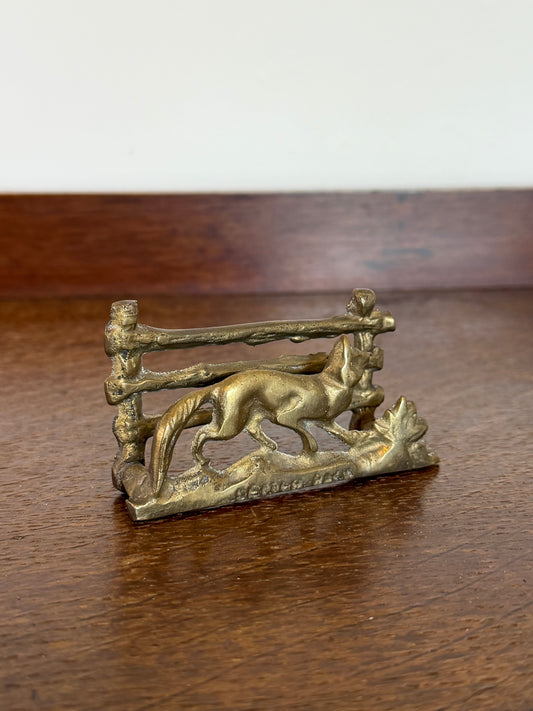 A small vintage brass fox figurine with a rustic fence design, displayed on a polished wooden tabletop.