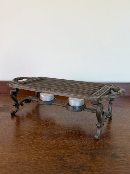 Vintage cast iron tealight food warmer with decorative scroll legs and handles.