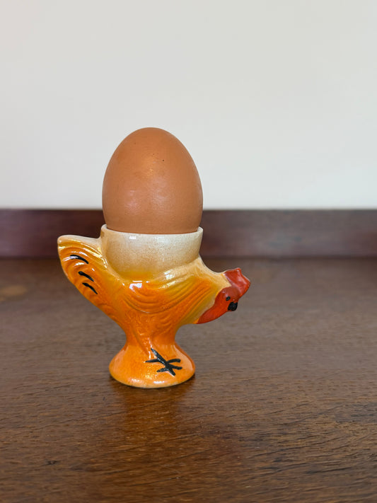Vintage orange ceramic chicken-shaped egg cup with cream egg holder, red comb, black feet and glossy painted finish.
