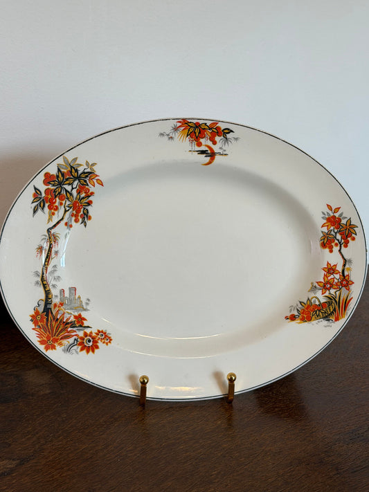 An oval white porcelain serving platter with a delicate hand-painted floral border in orange, green, and black, displayed on a dark wooden surface.