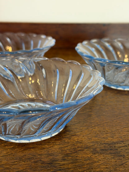 Three clear blue vintage glass bowls with a ribbed, scalloped rim, arranged on a dark wooden surface.