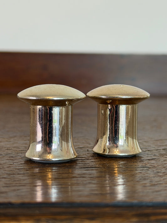 Pair of vintage silver-tone salt and pepper shakers with domed tops and flared bases on a wooden table.