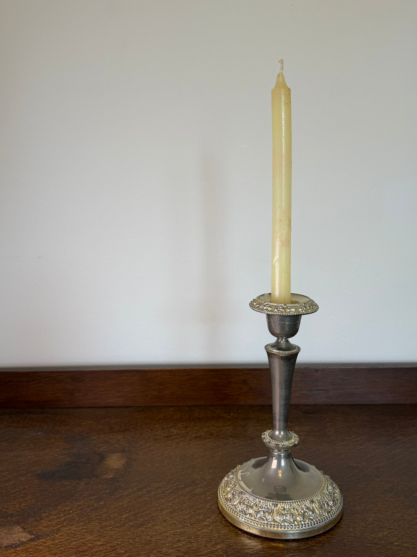 Vintage English silver plated candlestick with ornate embossed detailing holding a cream dinner candle.