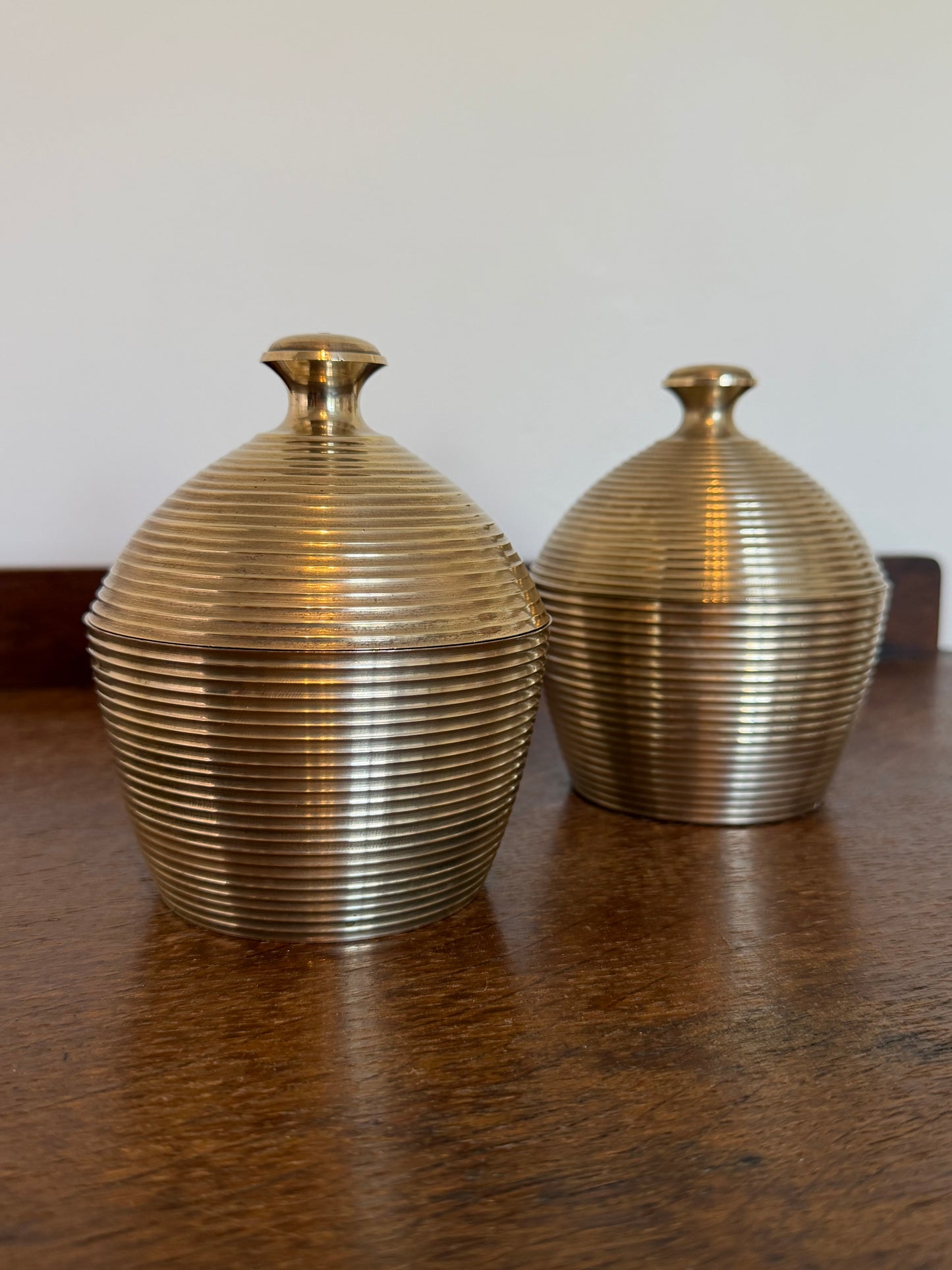 Two ribbed vintage made in India metallic brass acorn-shaped decorative containers with lids, shown on a dark wooden surface against a plain light background.