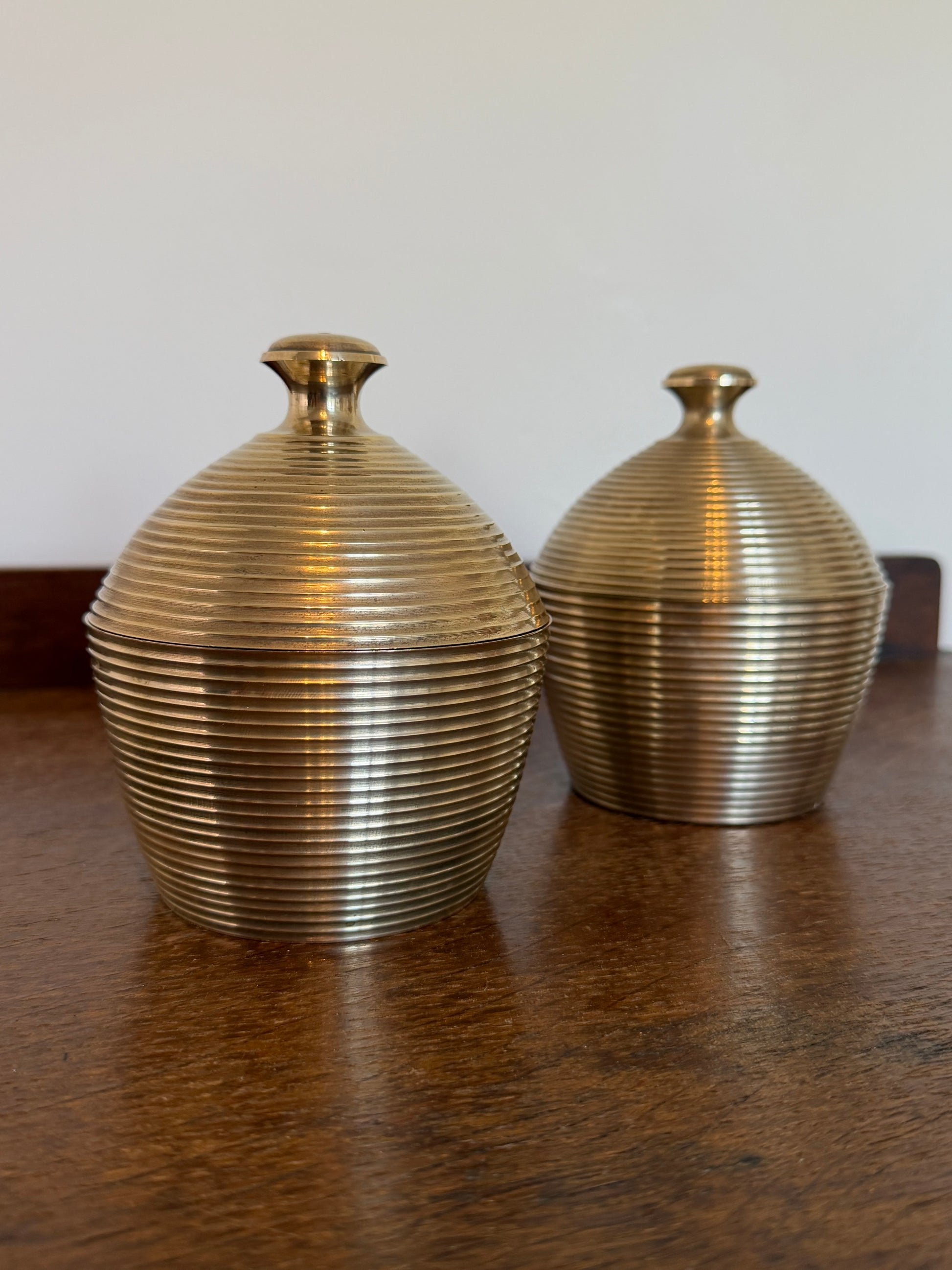 Two ribbed vintage made in India metallic brass acorn-shaped decorative containers with lids, shown on a dark wooden surface against a plain light background.