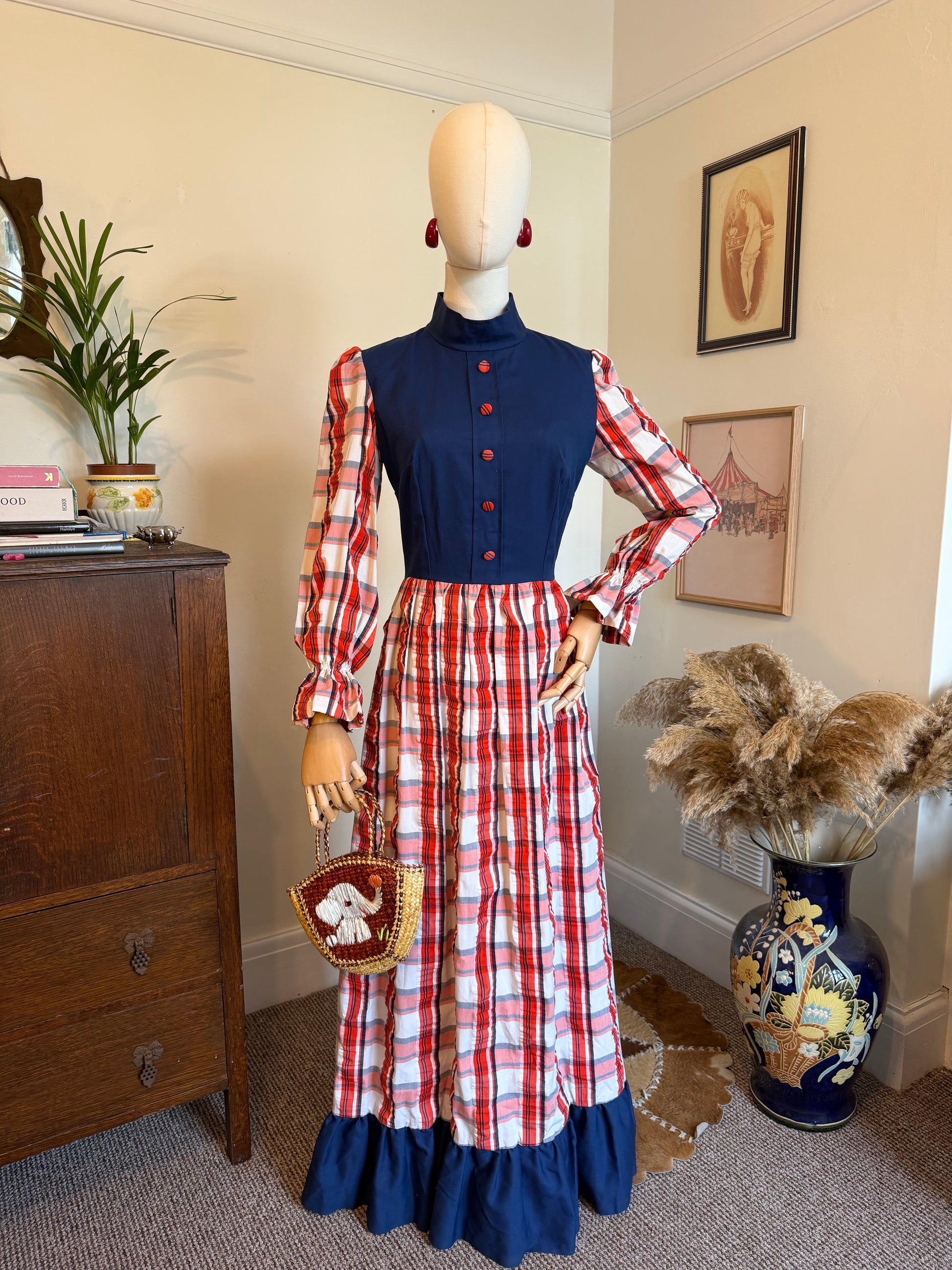 Vintage handmade 1970s prairie maxi dress with a navy bodice, red and white plaid skirt and sleeves, balloon sleeves, high neckline and navy ruffle hem displayed on a mannequin.