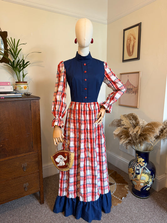 Vintage handmade 1970s prairie maxi dress with a navy bodice, red and white plaid skirt and sleeves, balloon sleeves, high neckline and navy ruffle hem displayed on a mannequin.